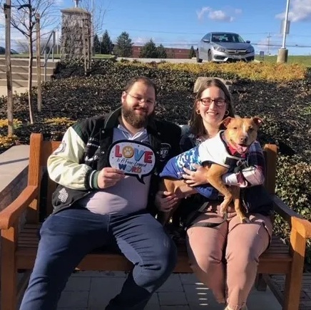 Couple holding dog on bench.